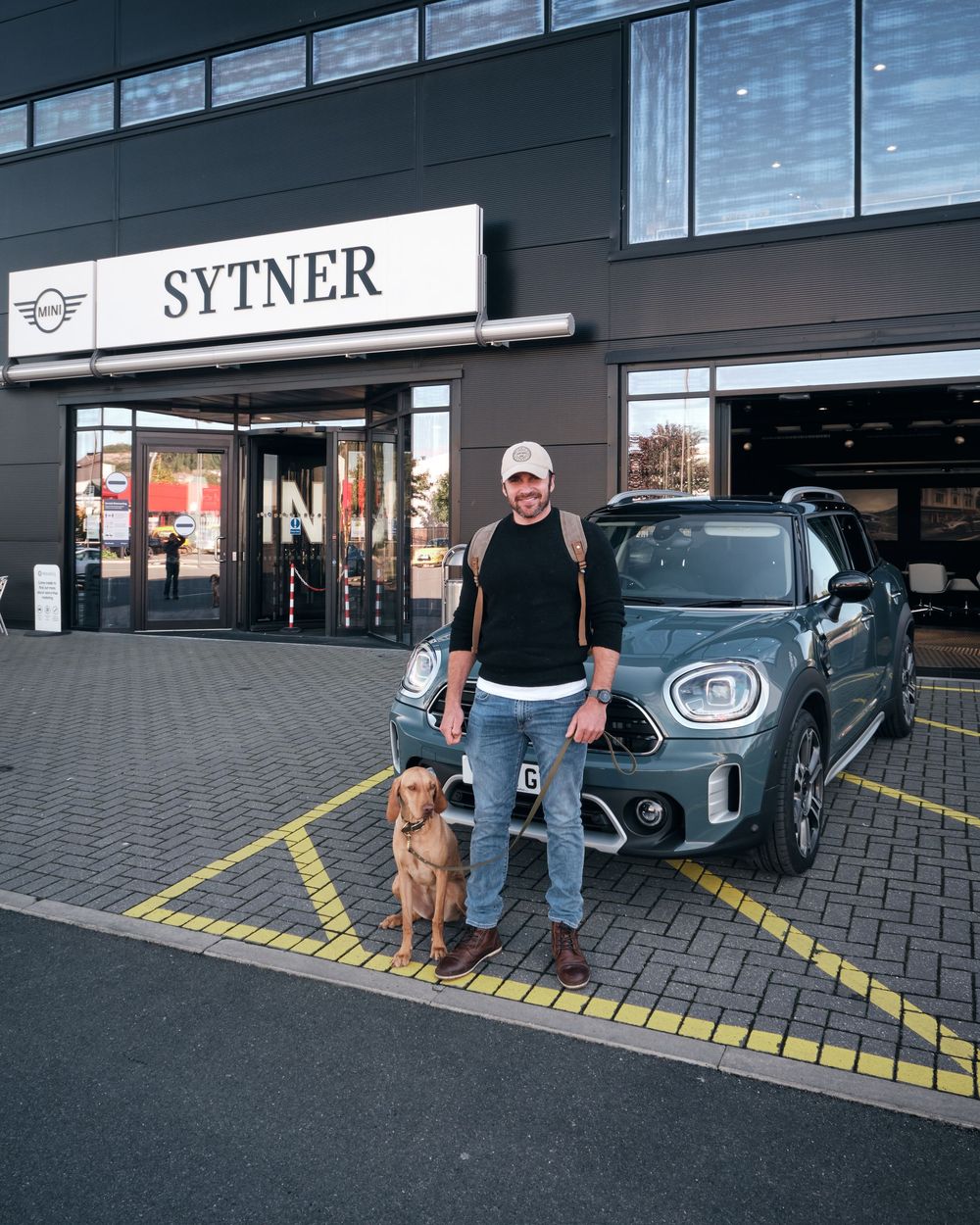 Man and dog posing with a MINI Countryman outside Sytner dealership.