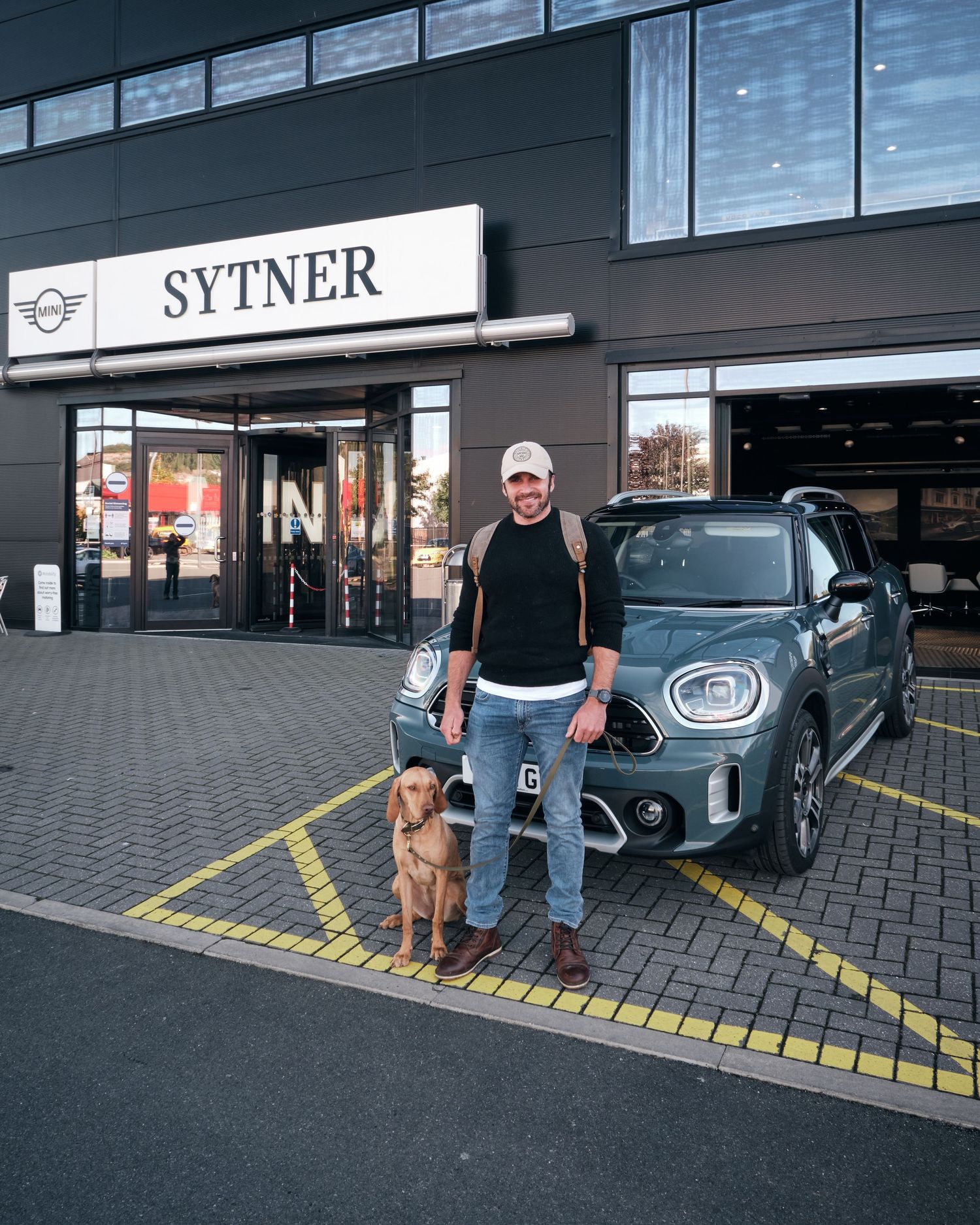 Man and dog posing with a MINI Countryman outside Sytner dealership.