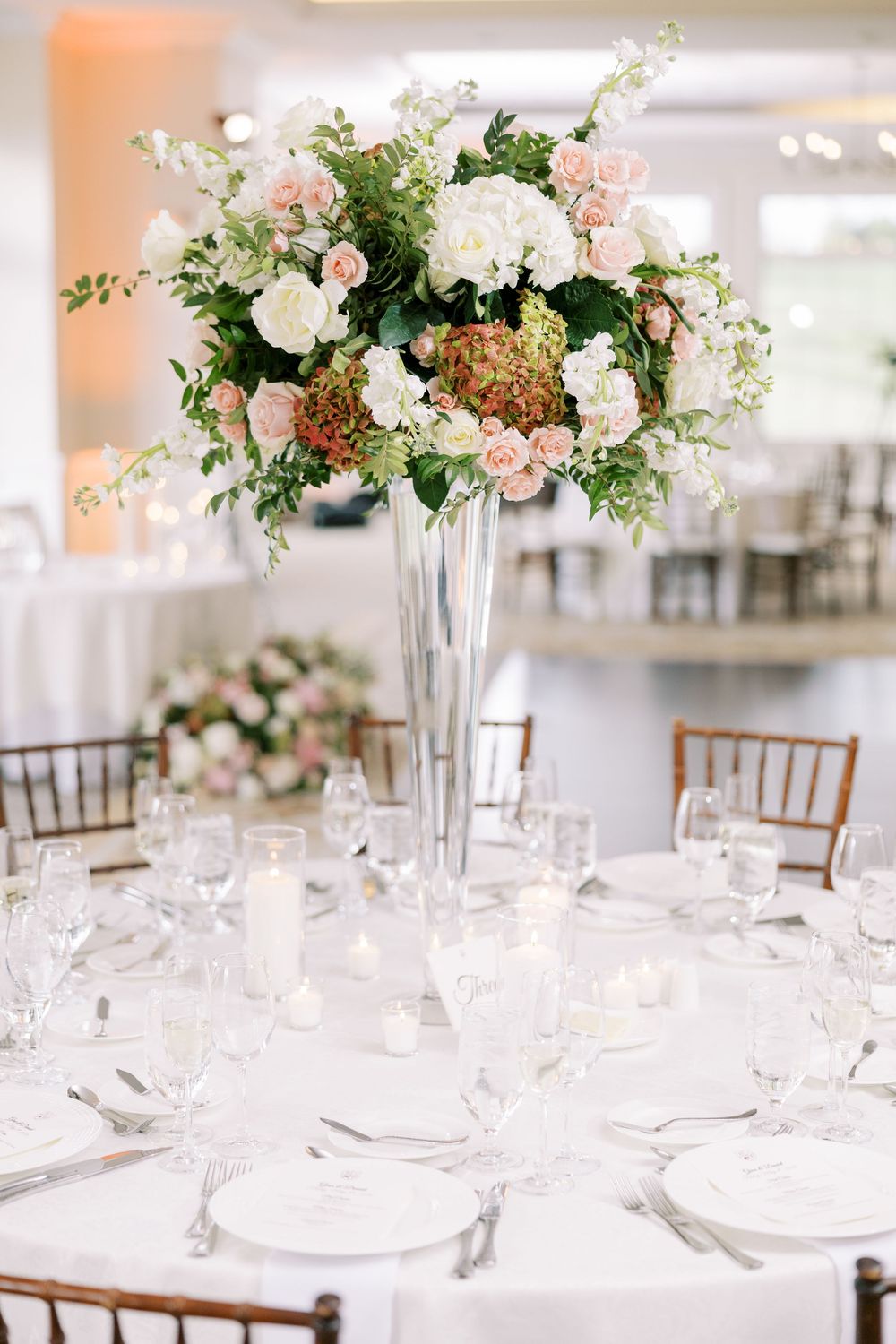 Elegant wedding reception table with tall silver vase centerpiece of blush roses and white hydrangeas.