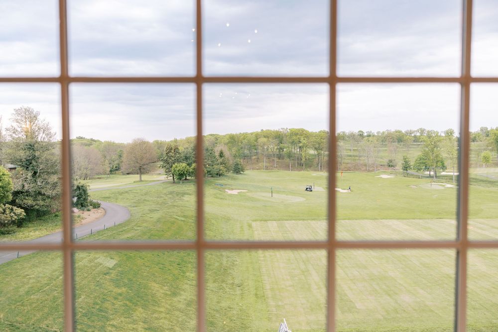 View through a multi-pane window overlooking a lush green golf course with trees under a cloudy sky.