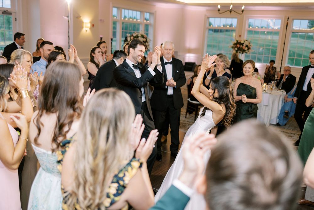 Bride and groom enter wedding reception as guests clap and celebrate on the dance floor.