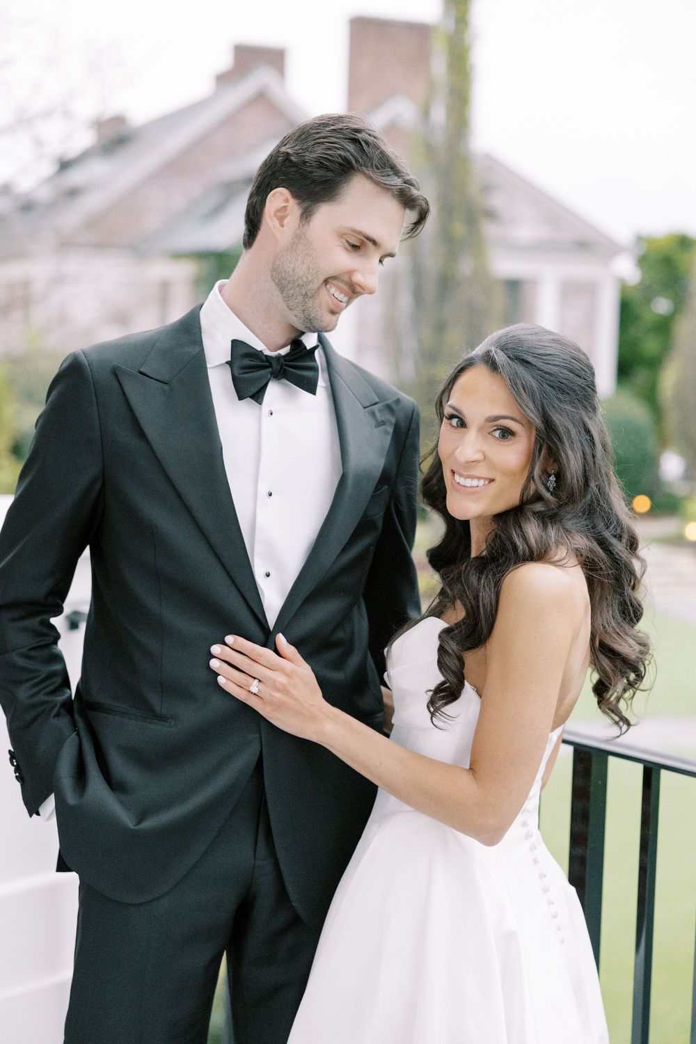 Elegant bride and groom pose outdoors, she in strapless gown, he in black tuxedo with bow tie.