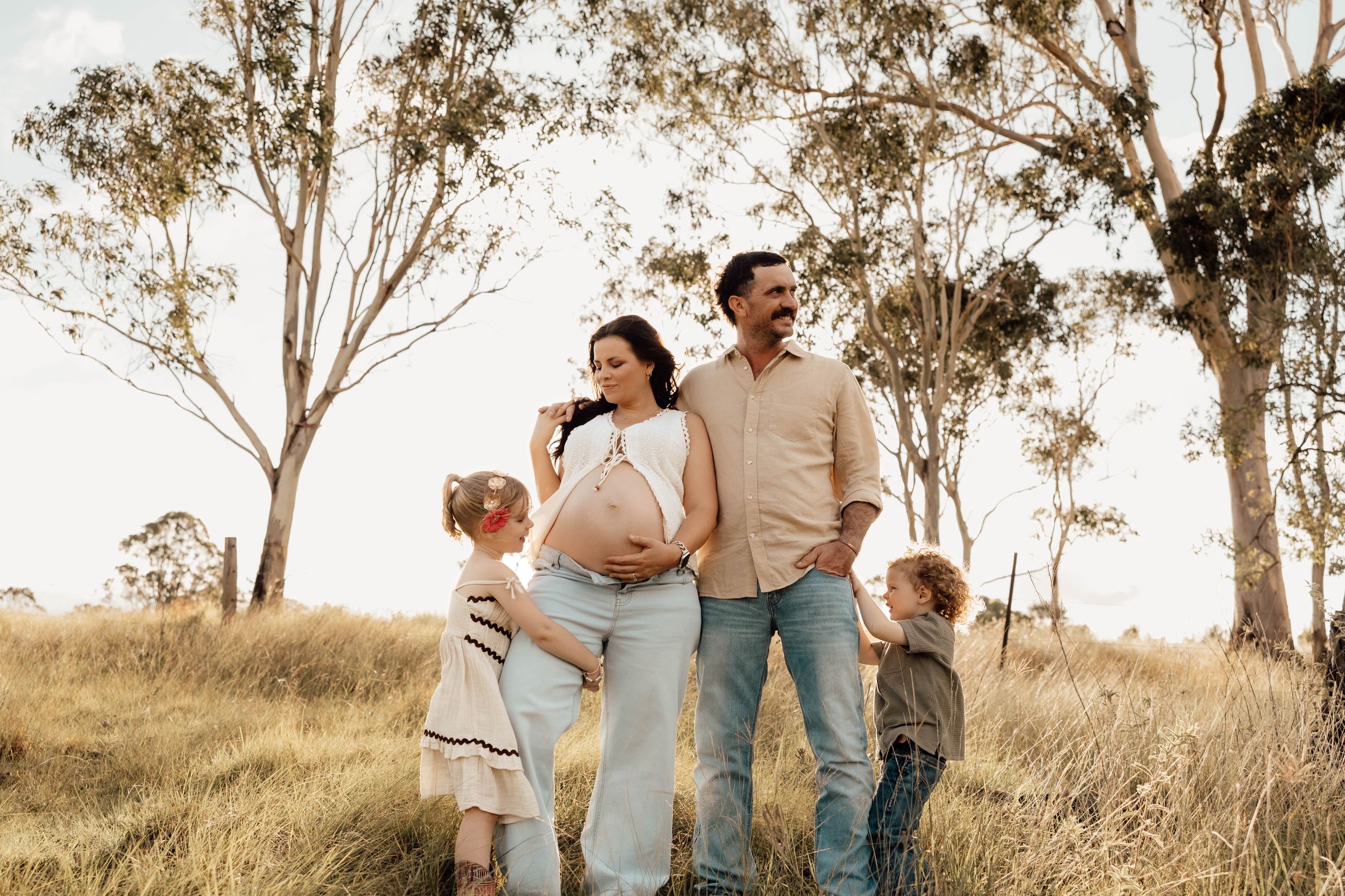 Pregnant woman with family standing in golden grass field surrounded by eucalyptus trees in Australia.