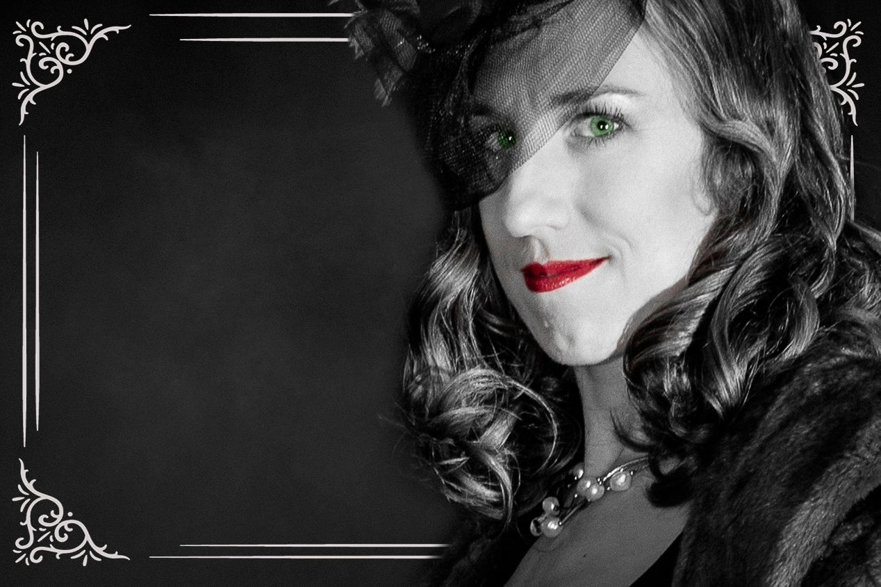 Black and white portrait of a woman with striking green eyes and red lips, wearing a fur coat and pearl necklace.