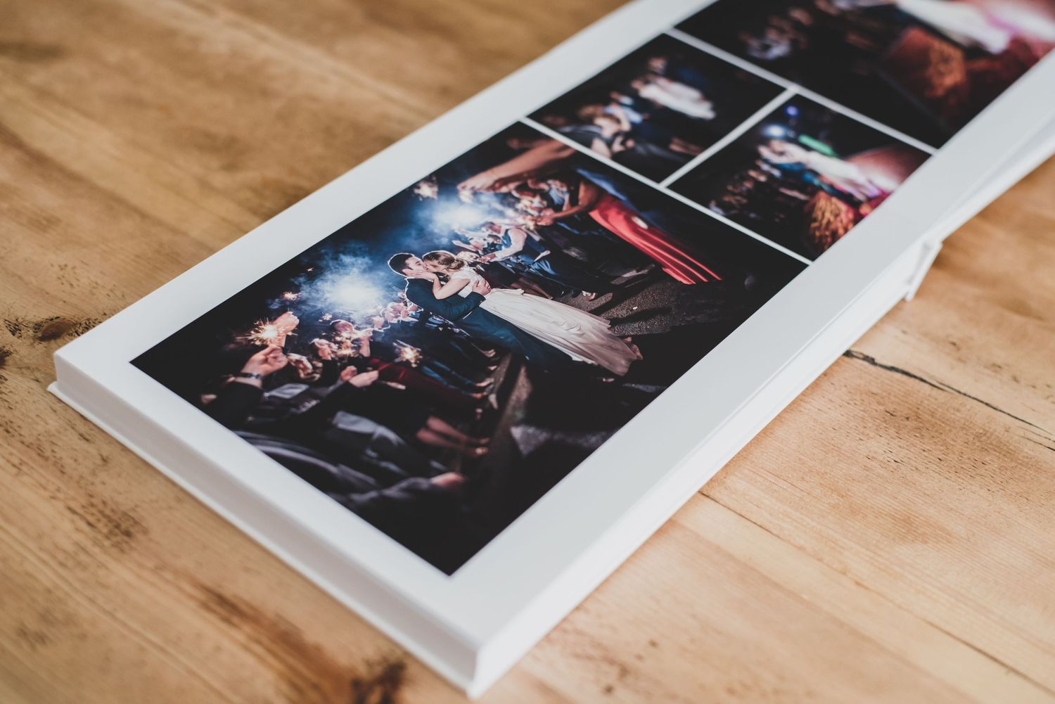 A white photo book displaying vibrant party and event photographs resting on a wooden surface.