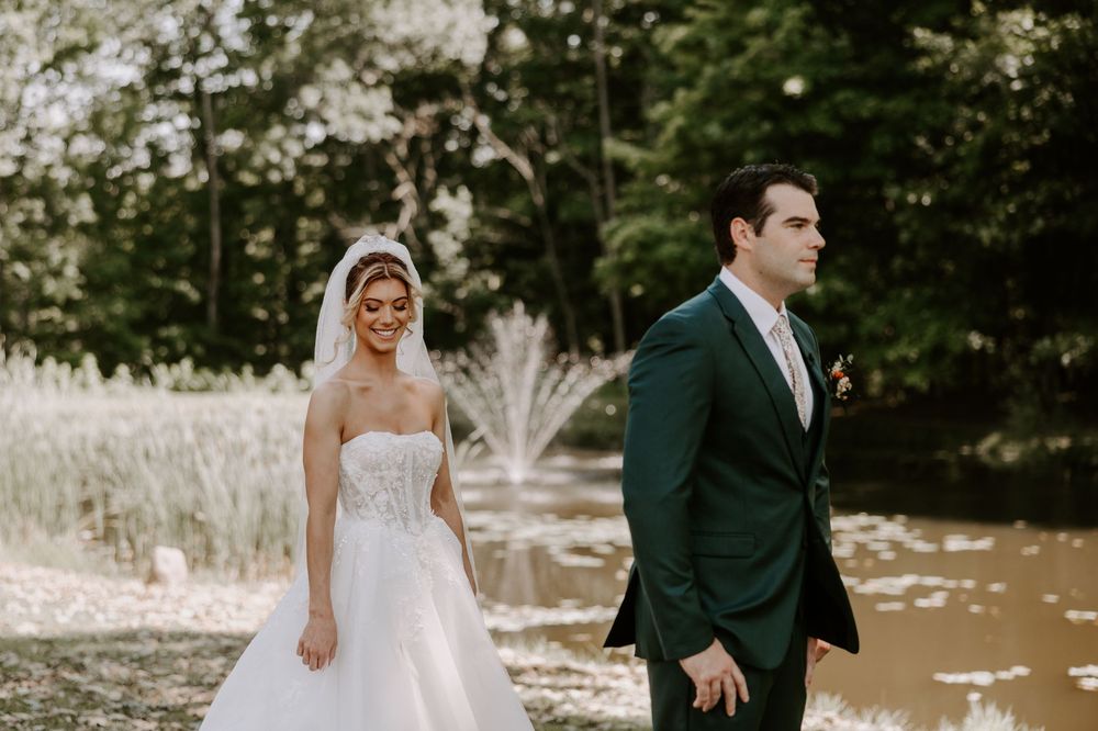 Bride in strapless gown and groom in green suit share first look moment by fountain.