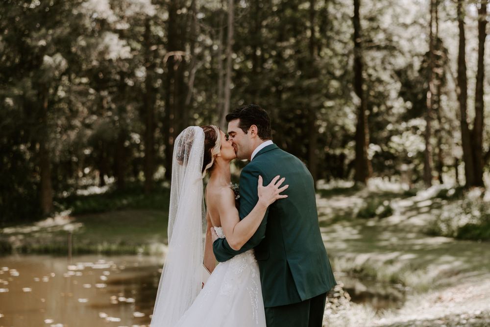 Bride and groom sharing a kiss outdoors surrounded by lush green forest trees.