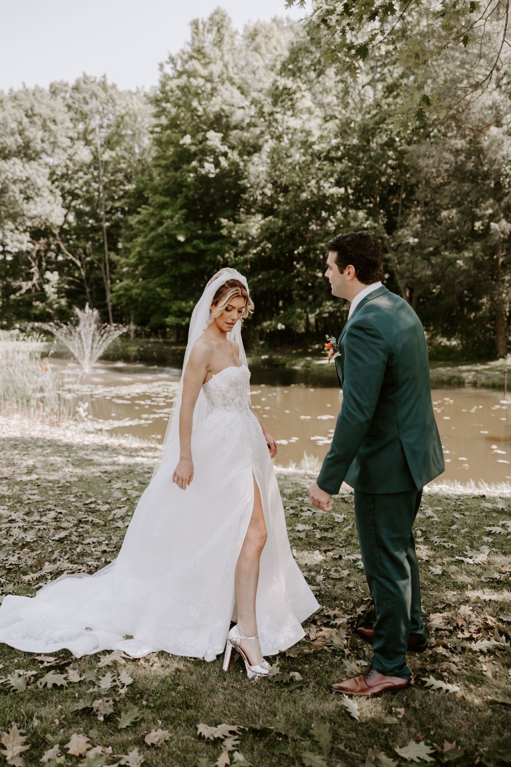 Bride lifts her gown hem while groom holds her hand near a serene garden fountain.
