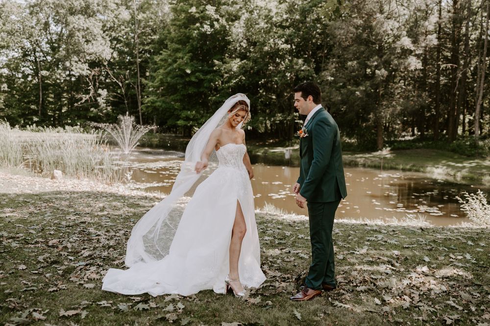Bride and groom share a romantic moment holding hands near a tranquil woodland pond.
