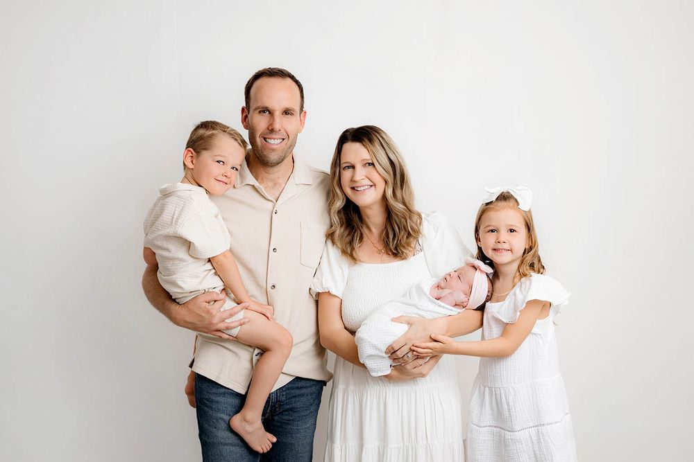 Family of five with newborn baby posing together smiling against a white studio background by Lake Elsinore family and newborn photographer.