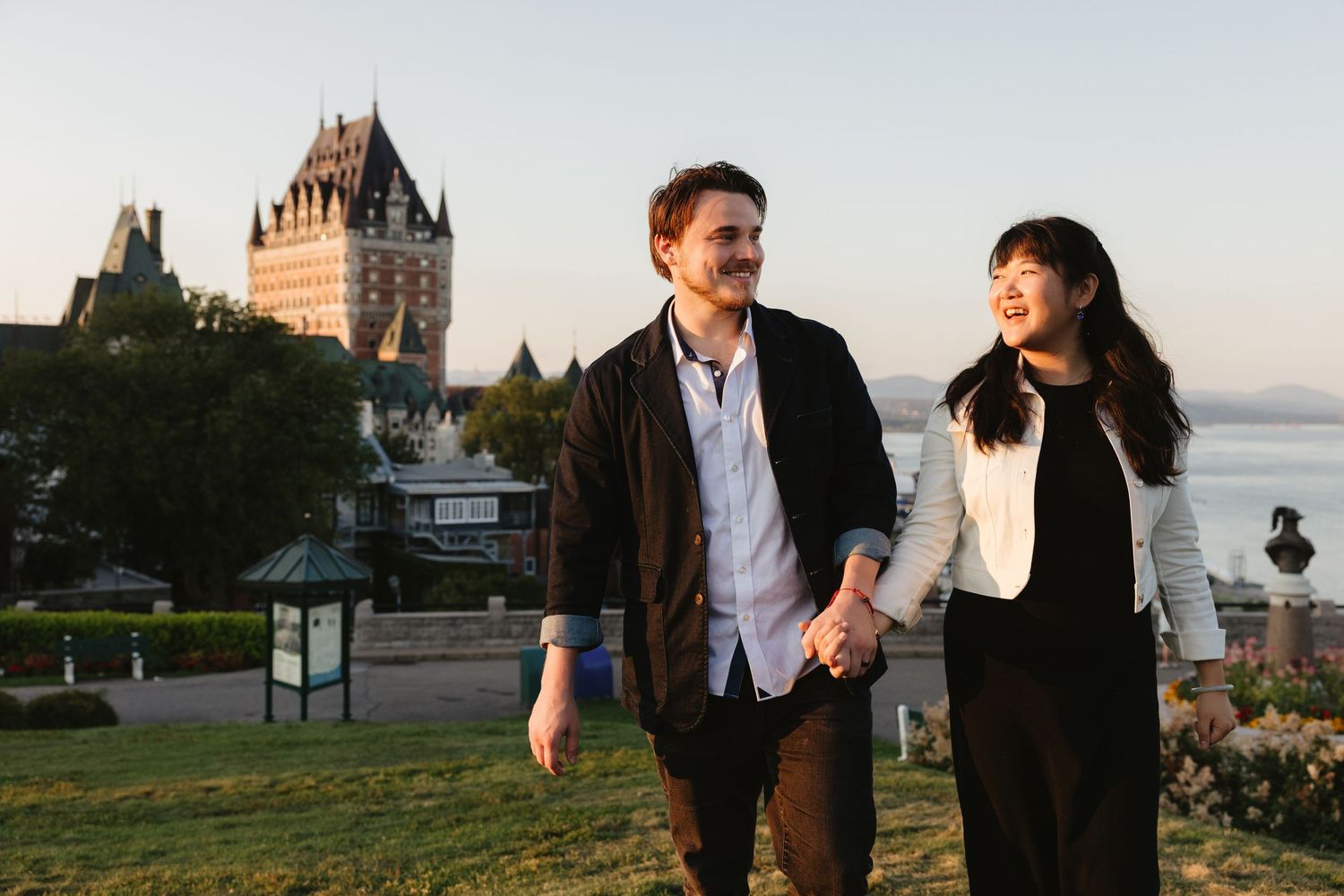 Couple holding hands walking outdoors with Chateau Frontenac and St. Lawrence River in Quebec City background.