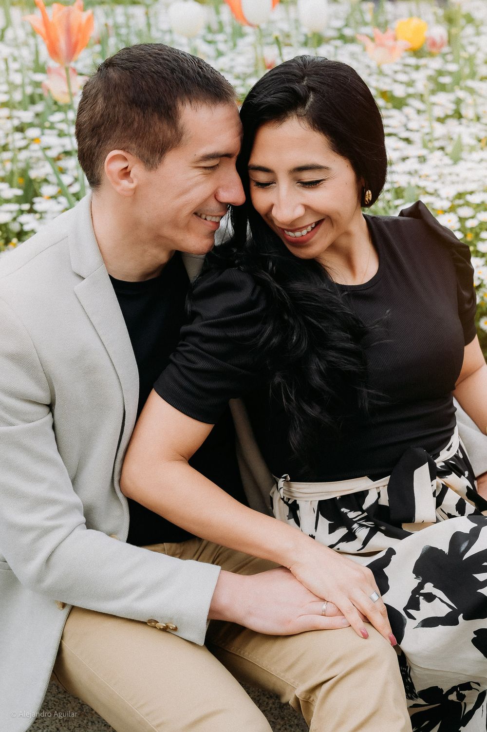 Joyful couple sitting close together smiling in a field of colorful spring flowers.