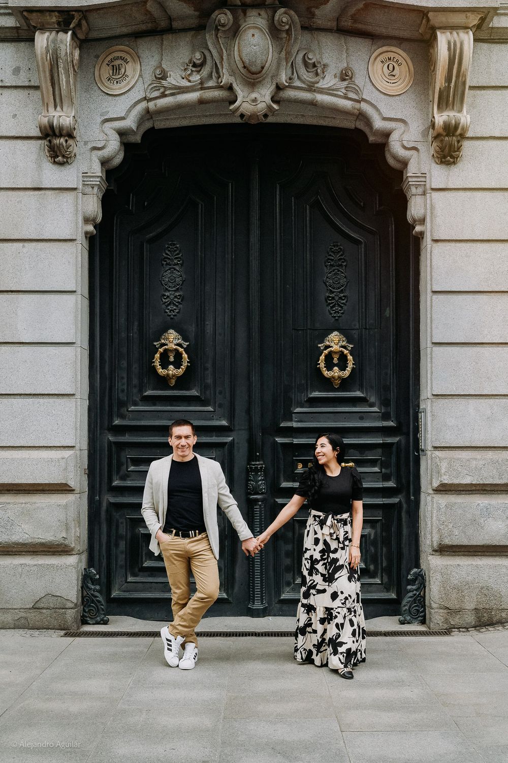 Couple holding hands before an ornate dark wooden door with gold details.