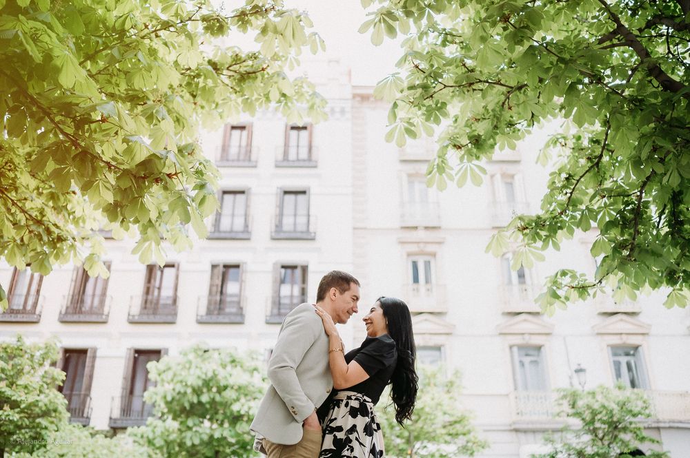 Couple sharing a romantic kiss beneath lush green trees in Madrid.