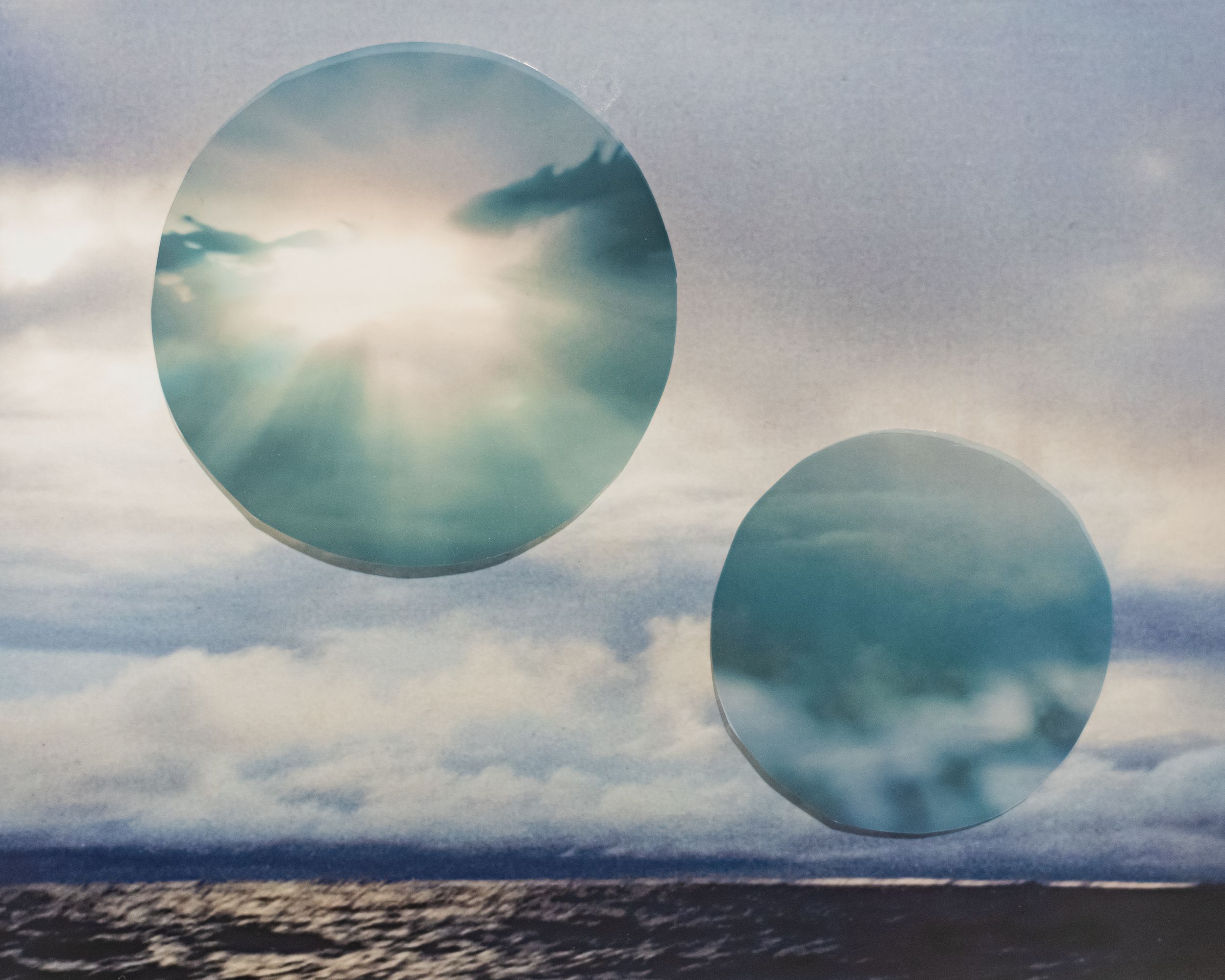 Two luminous circular orbs float over a dramatic seascape with stormy clouds and bright sunlight.
