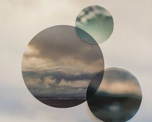 Three overlapping circular frames reveal a dramatic cloudy landscape in a surreal photographic collage artwork.