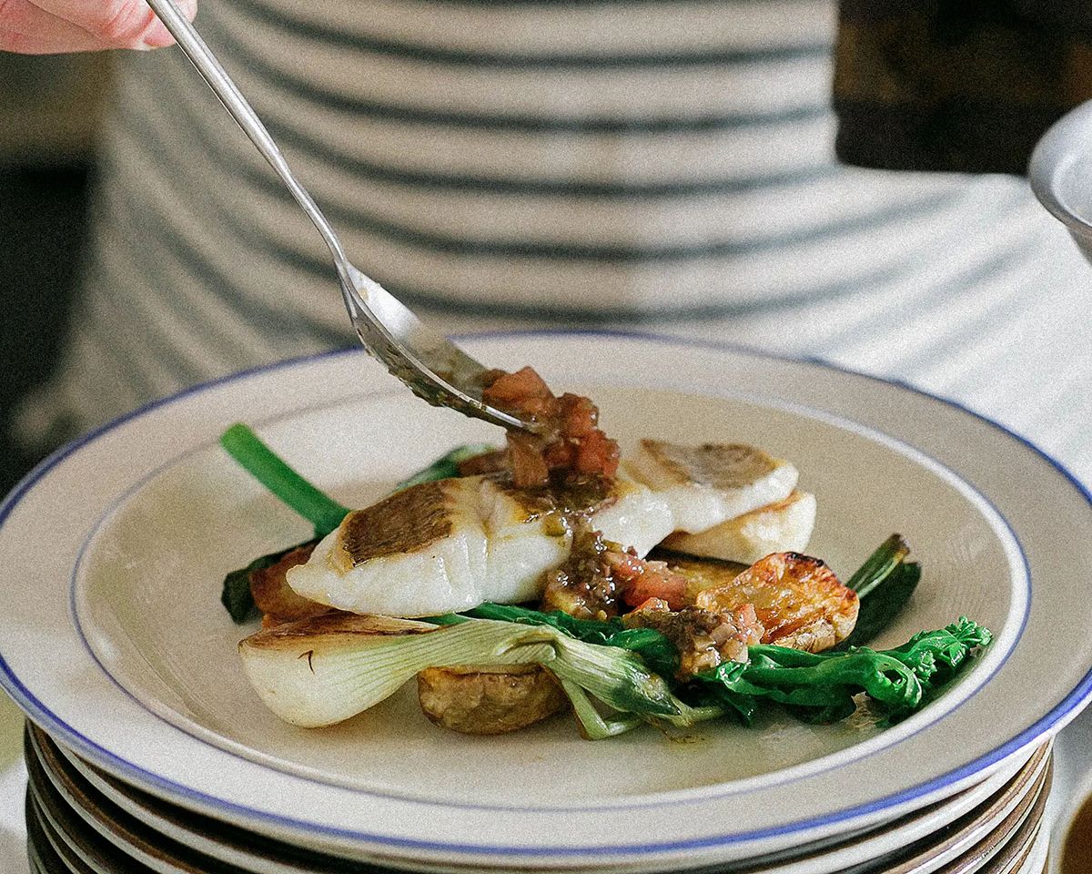 Elegant plated fish dish with bok choy, tomato relish, and greens on a white rimmed plate, garnished with a fork.