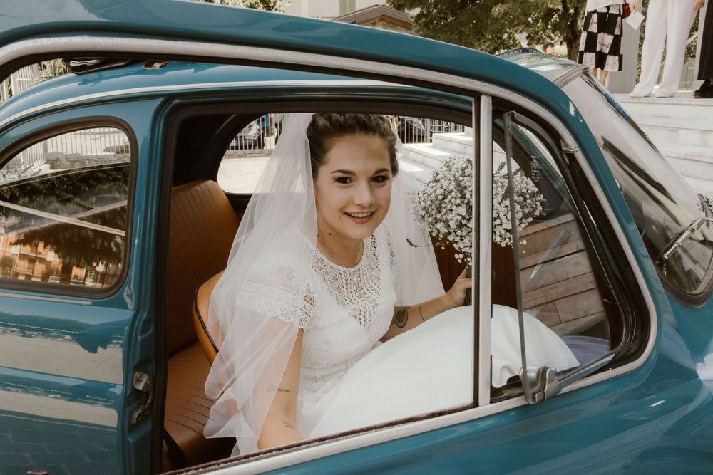 Beautiful bride in white wedding dress and veil smiling inside a vintage blue classic car.