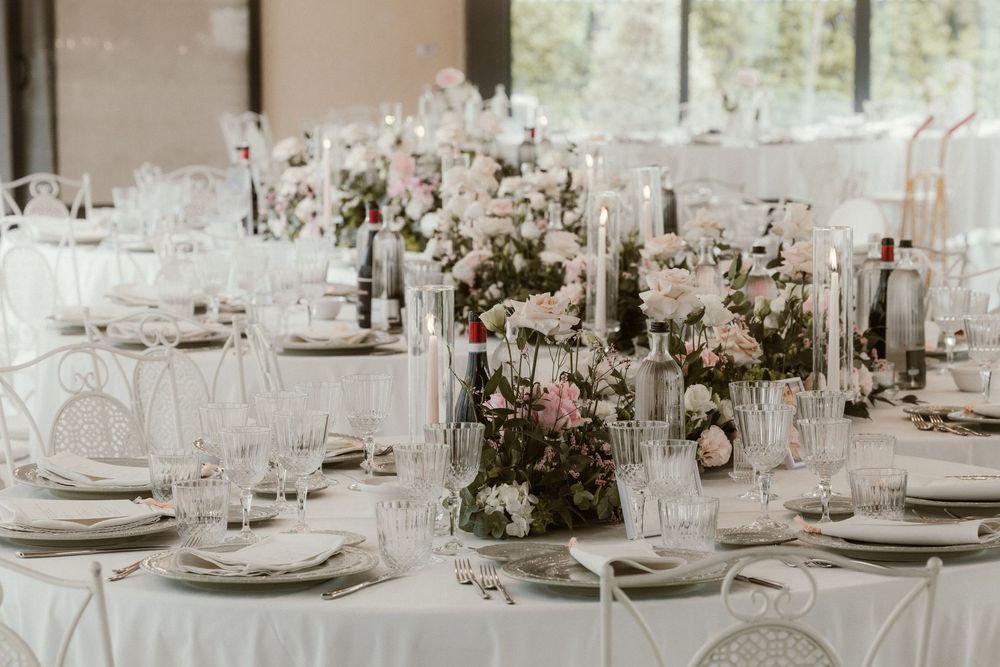 Elegant wedding reception table with white linens, crystal glassware, pink floral centerpieces, and tall taper candles.