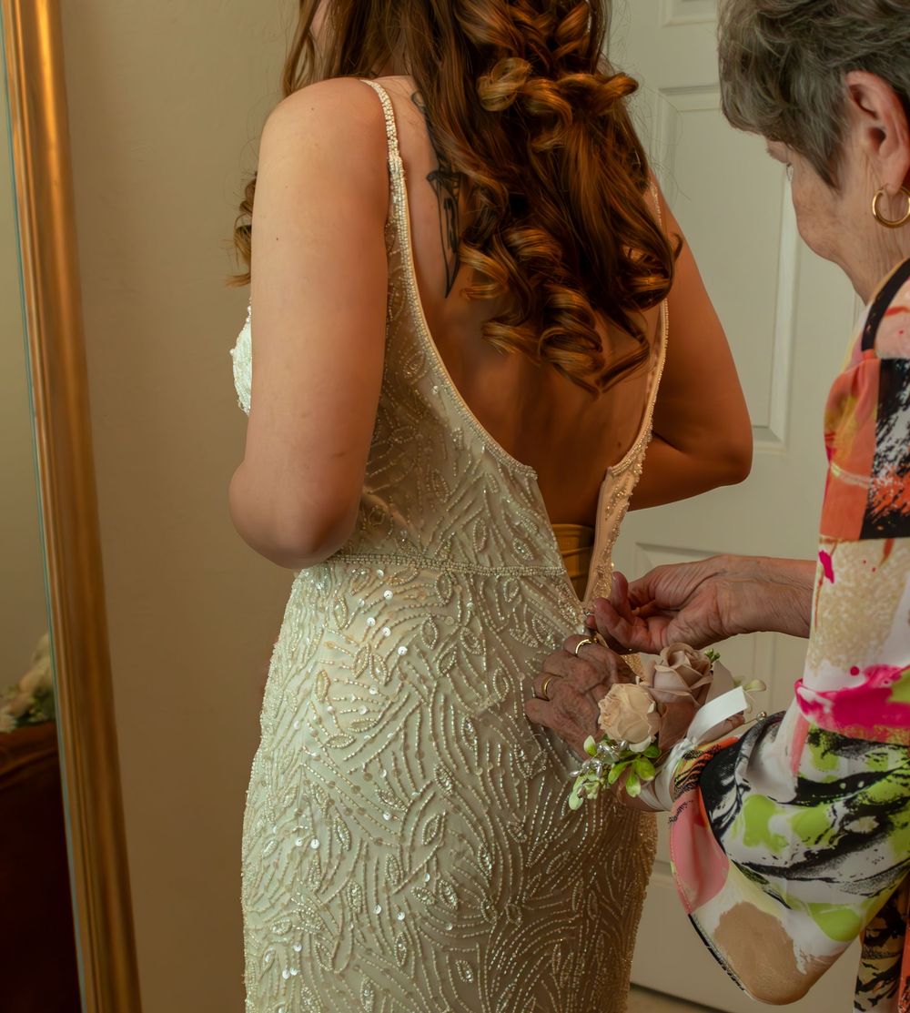 Young woman in a backless sequined gown gets corsage pinned by older woman, elegant updo hairstyle.
