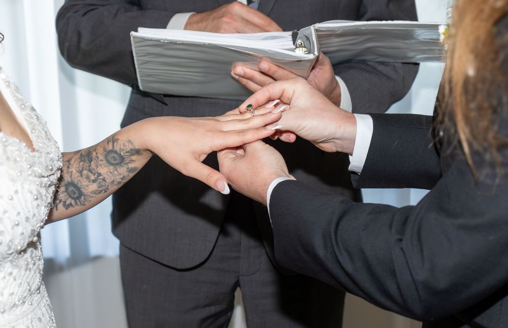 Close-up of wedding ring exchange ceremony with tattooed bride and groom hands held by officiant.
