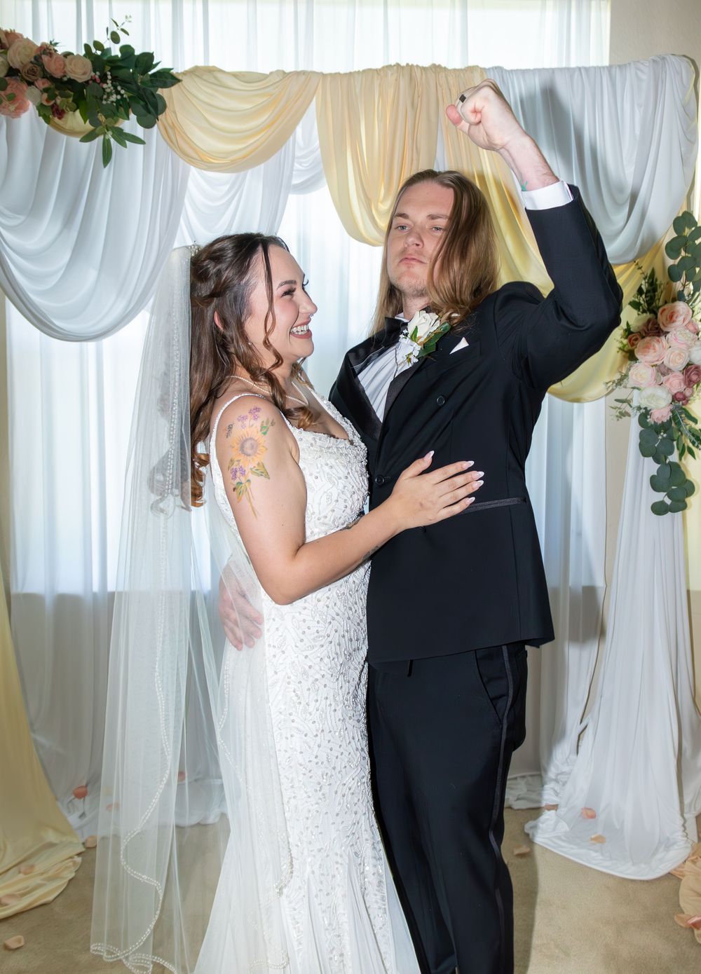Newlywed couple celebrating at wedding altar, groom raising fist in joy beside smiling tattooed bride.