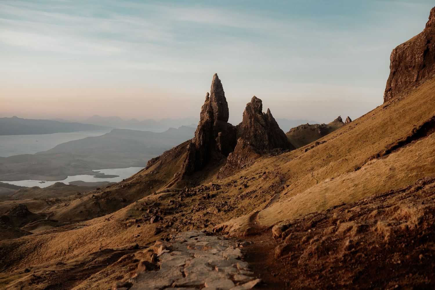 Dramatic rocky pinnacles of the Old Man of Storr rise above golden moorland on the Isle of Skye at golden hour.