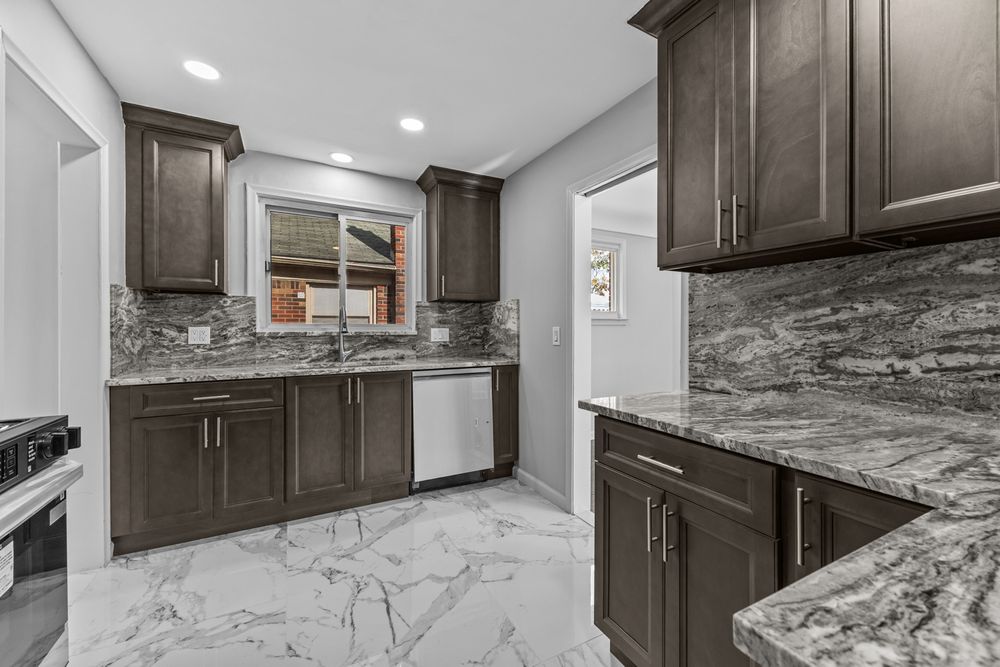 Renovated kitchen featuring dark cabinetry, granite backsplash, marble floors, and stainless steel dishwasher.