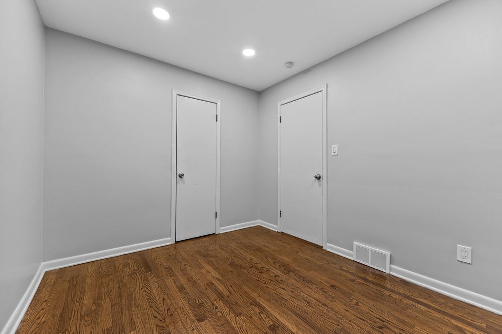 Bright empty room with hardwood floors, recessed lighting, and two white interior doors.