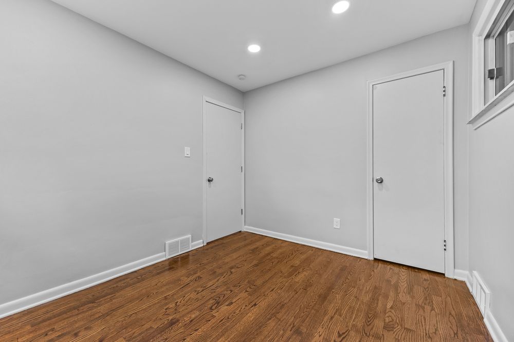 Spacious empty room featuring rich hardwood floors, white trim, recessed lighting, and a white door.