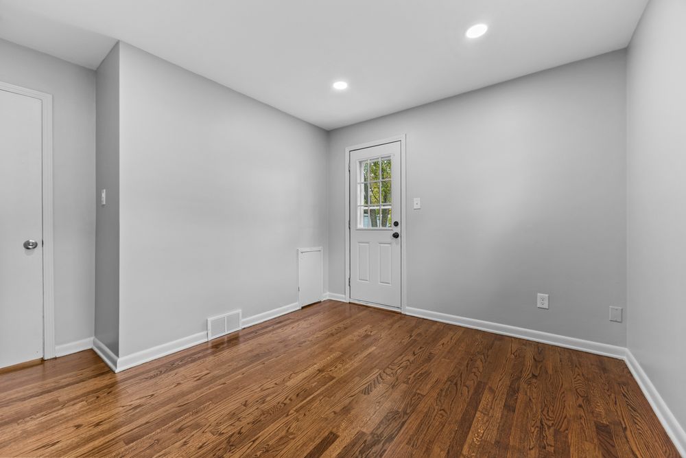Clean empty room with hardwood floors, white baseboards, recessed lighting, and a rear entry door.