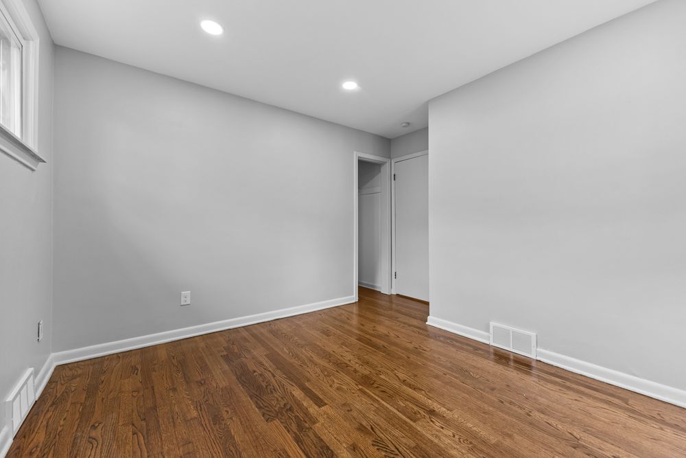 Minimalist empty room with warm hardwood floors, white walls, recessed lighting, and a closet door.
