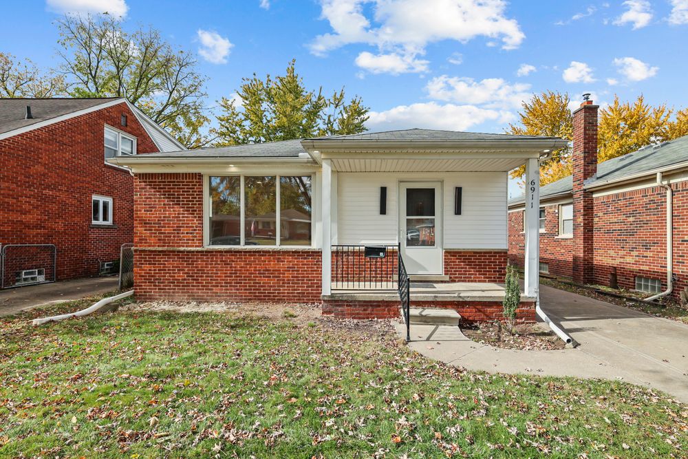 Brick ranch home with white trim, covered front porch, and mature trees in autumn setting.