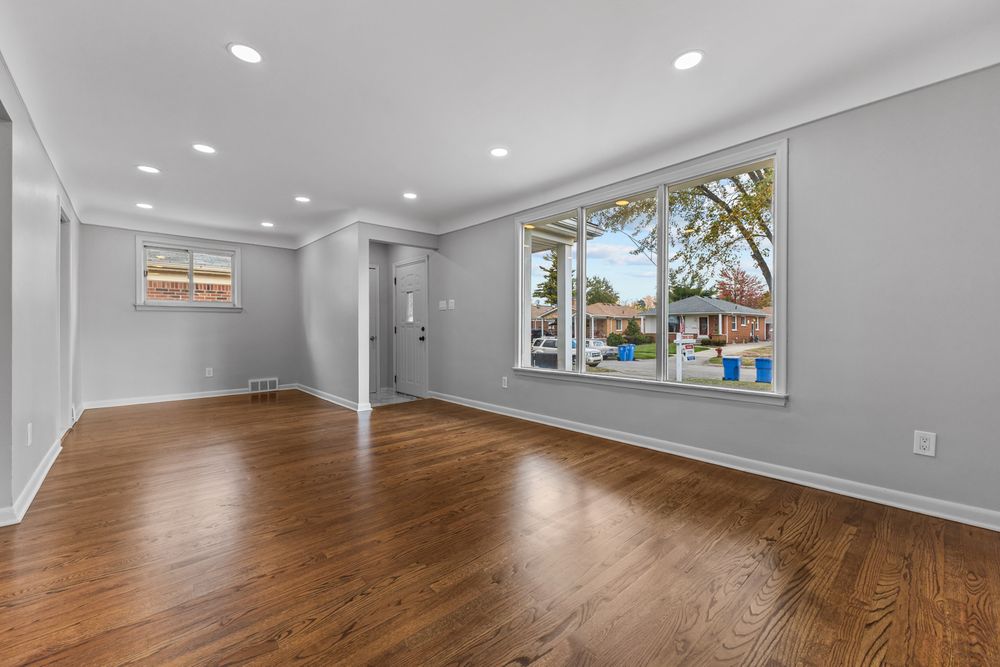 Open living area with rich hardwood floors, large windows, recessed lighting, and crown molding.