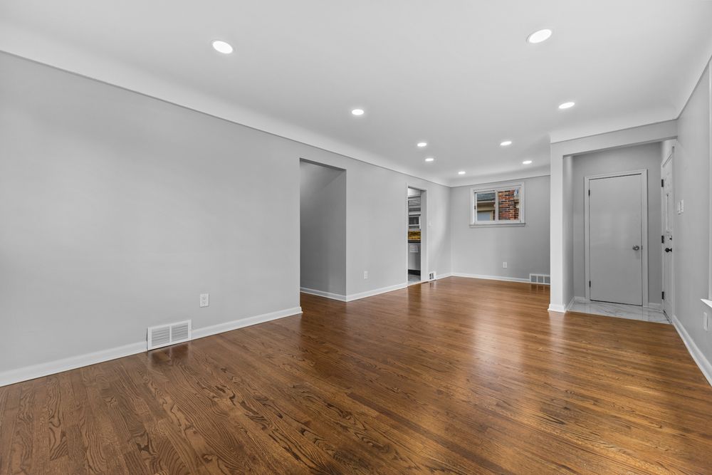 Spacious empty living room with hardwood floors, recessed lighting, crown molding, and neutral gray walls.