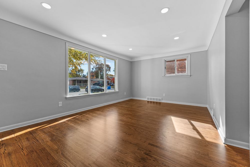 Bright empty room with hardwood floors, large window, recessed lighting, and crown molding details.