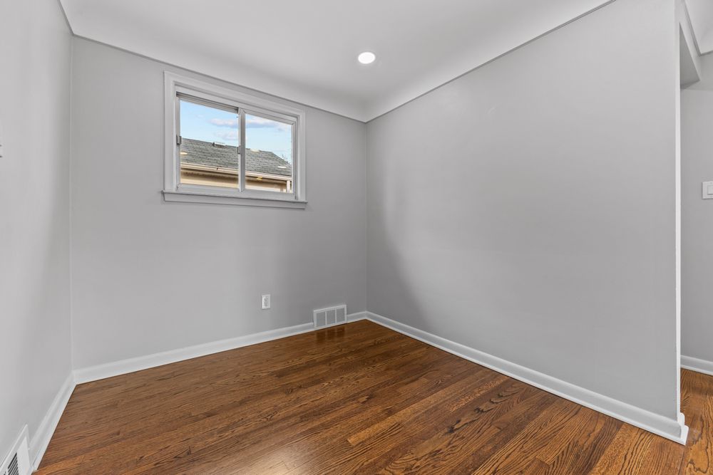 Small empty bedroom with hardwood floors, single window, recessed lighting, and neutral gray walls.