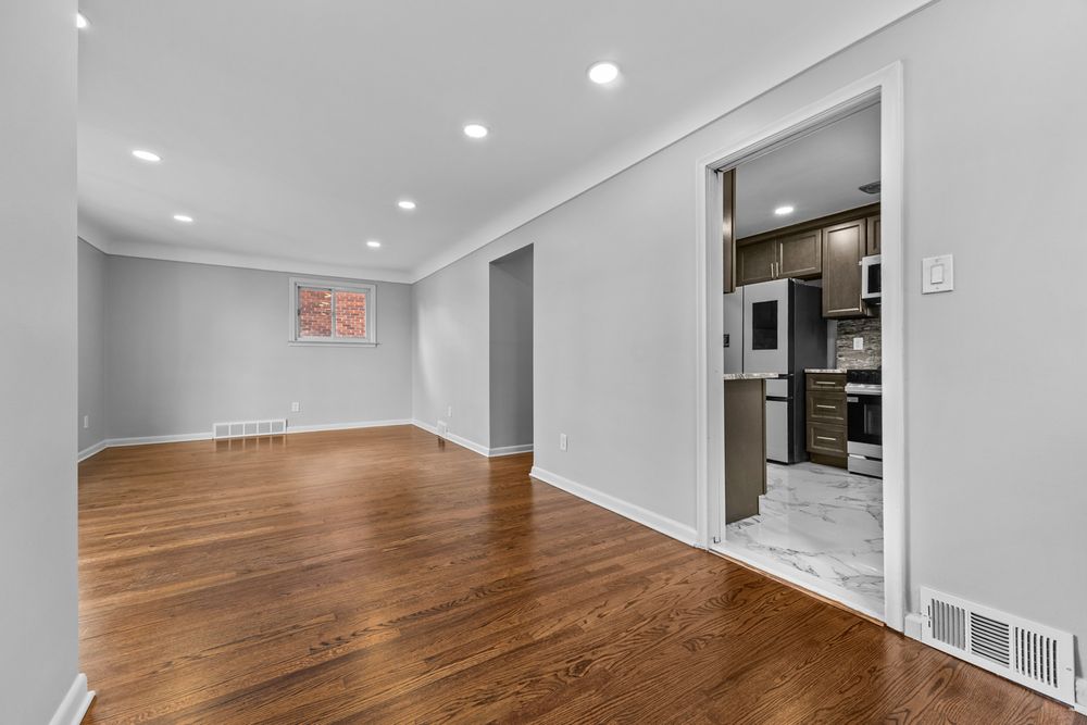 Open living space with hardwood floors, recessed lighting, crown molding, and view into modern kitchen.
