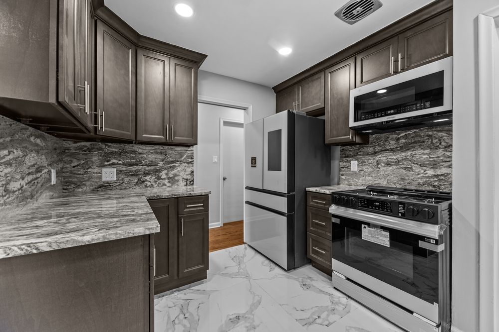 Modern kitchen with dark cabinets, marble backsplash, stainless steel appliances, and marble tile floors.