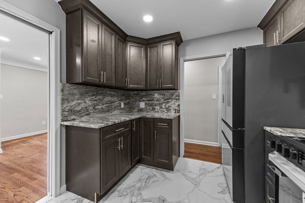 Corner kitchen with dark espresso cabinets, granite countertop backsplash, and marble tile flooring.
