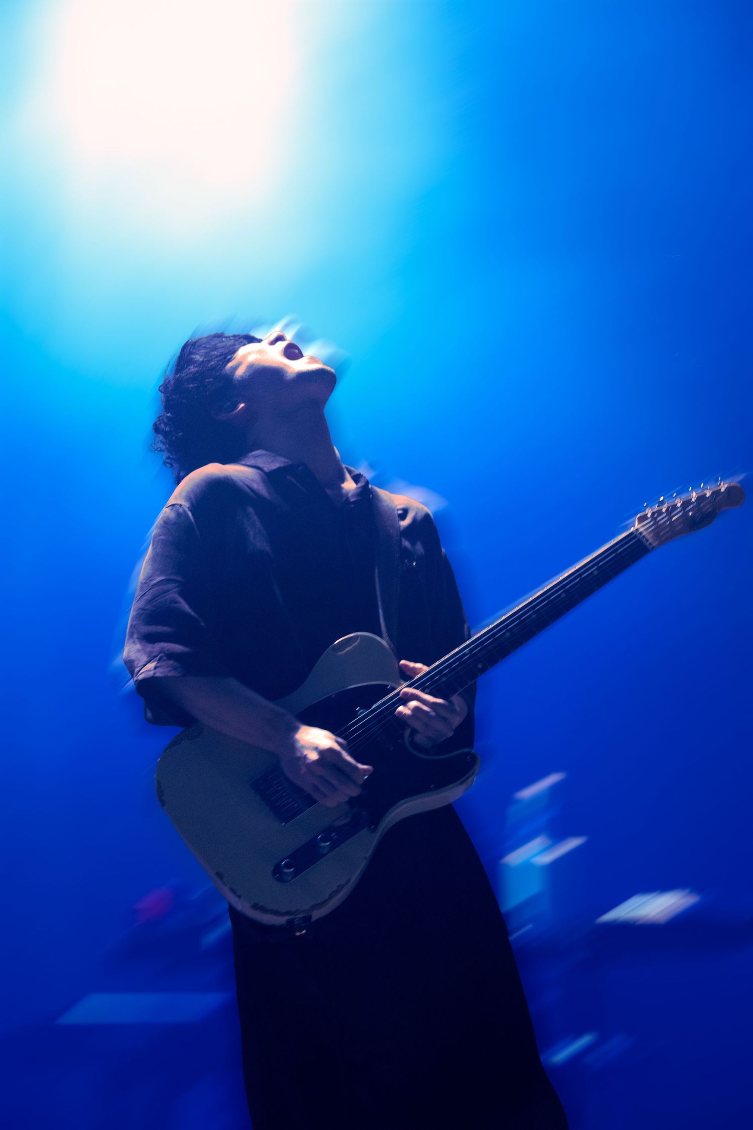 A photo of TK from Ling Tosite Sigure underneath blue concert lights during his performance at The Belasco