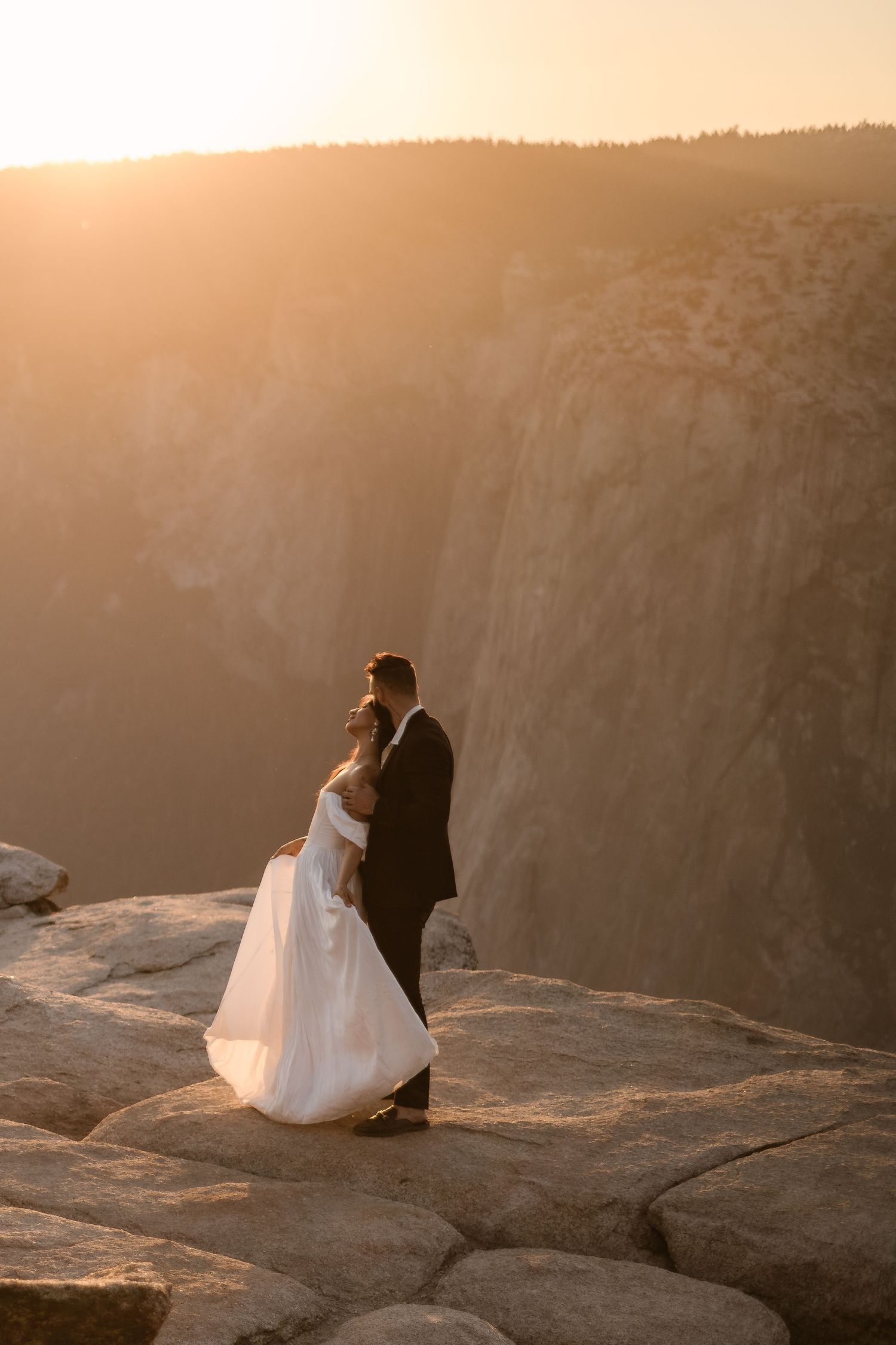 Wedding couple sitting on cliff edge during golden hour sunset.