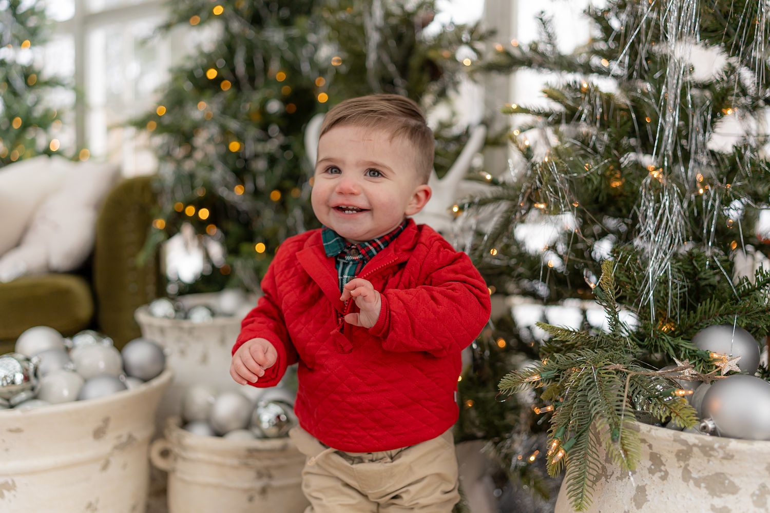 Baby in red sweater playing near decorated Christmas tree with twinkling lights.
