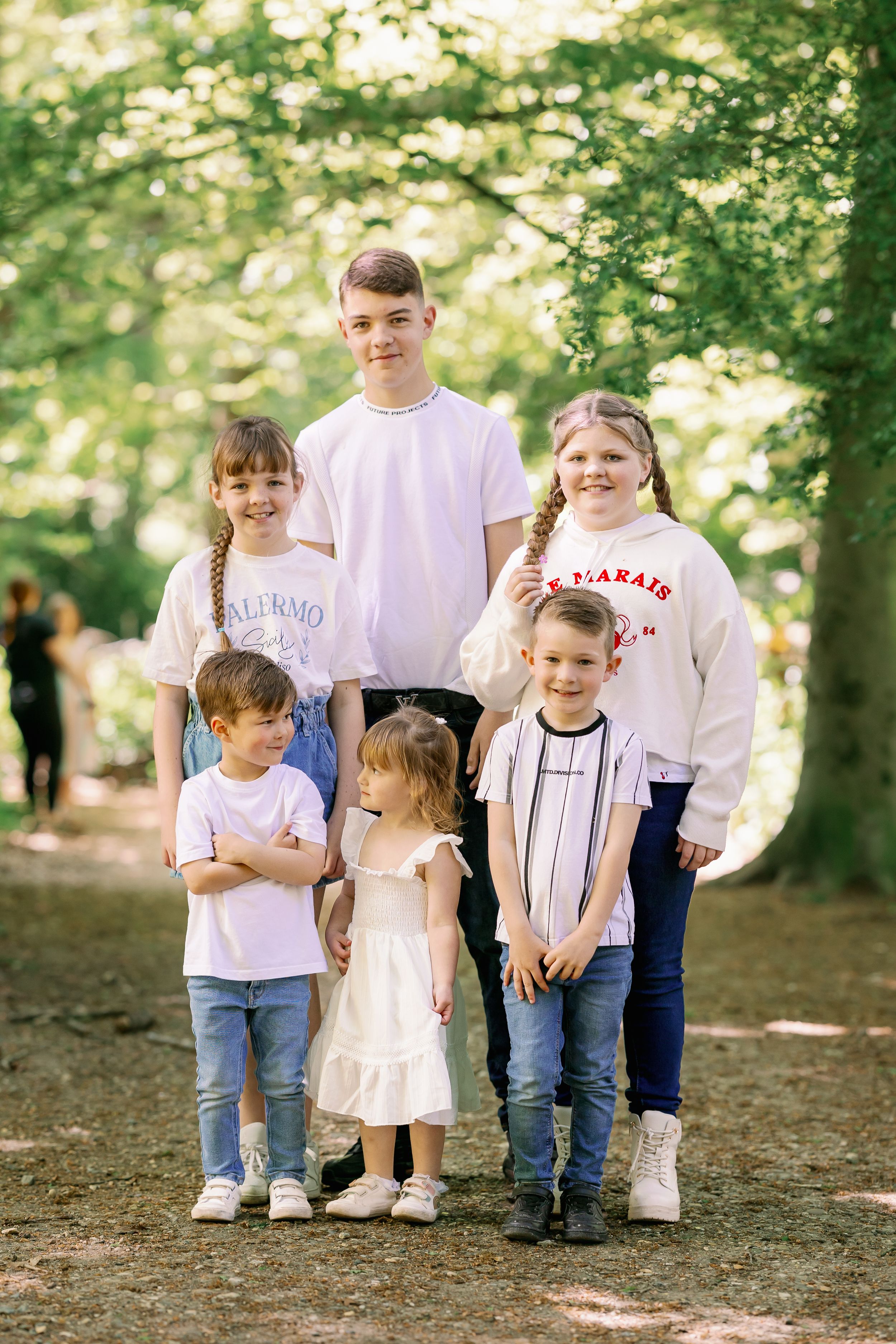 Group of children standing together outdoors in casual clothing against a natural wooded background.
