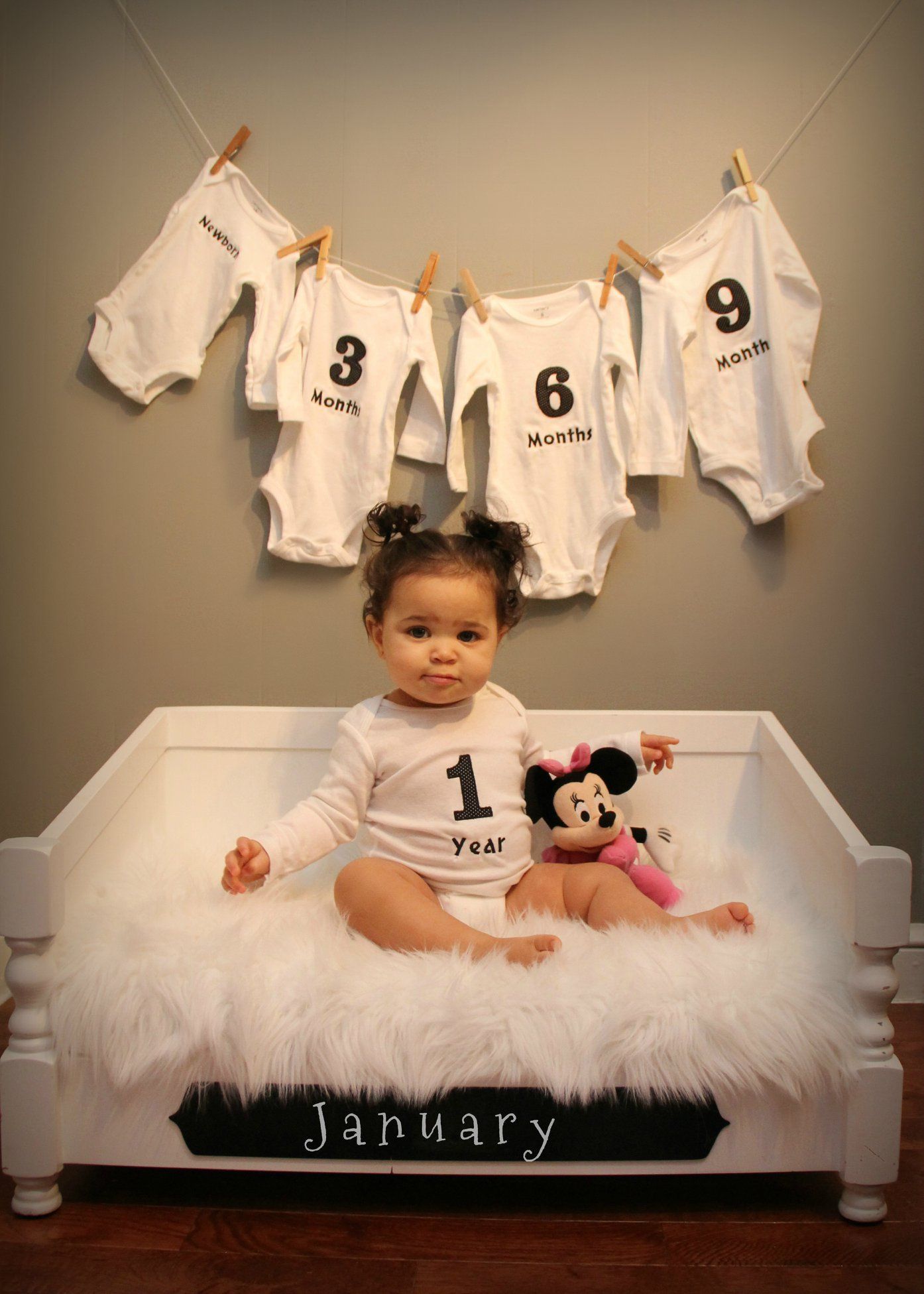 Baby photography setup with numbered onesies hanging on clothesline.