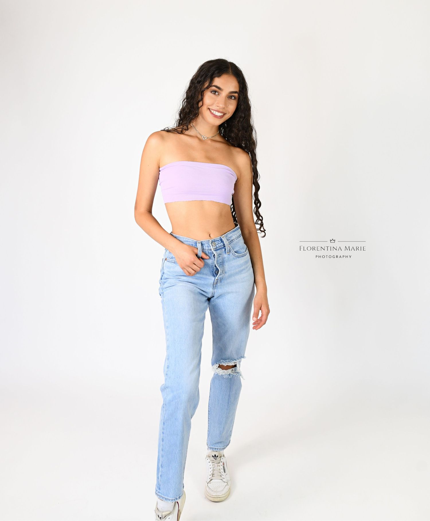 Fashion portrait in ripped jeans and pink crop top against white backdrop.