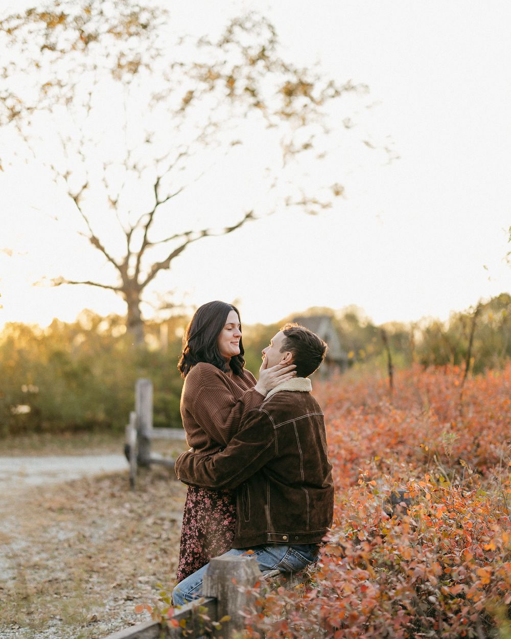 A couple embraces among colorful fall foliage at sunset.