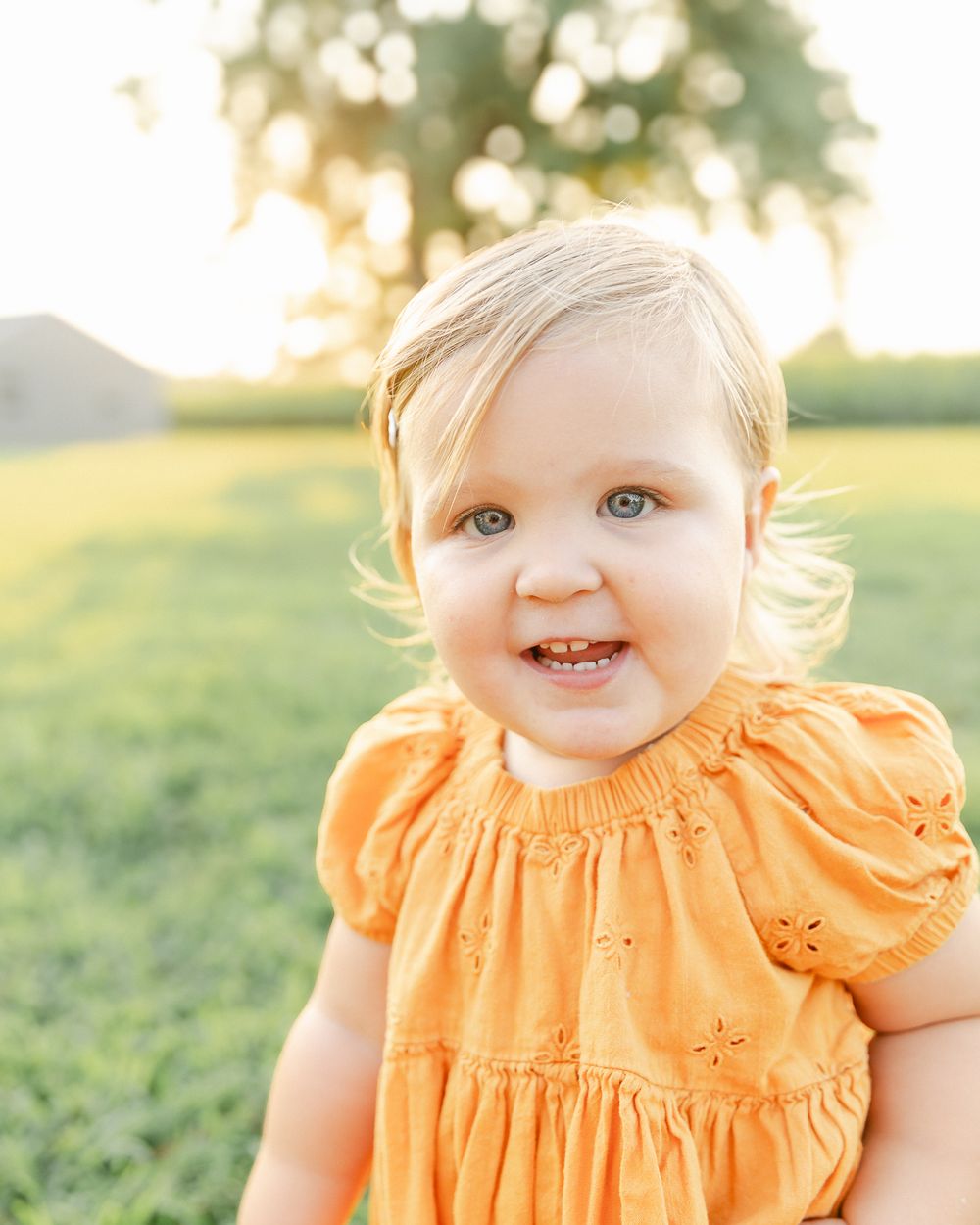 A child in an orange dress smiles brightly in a sunny field.
