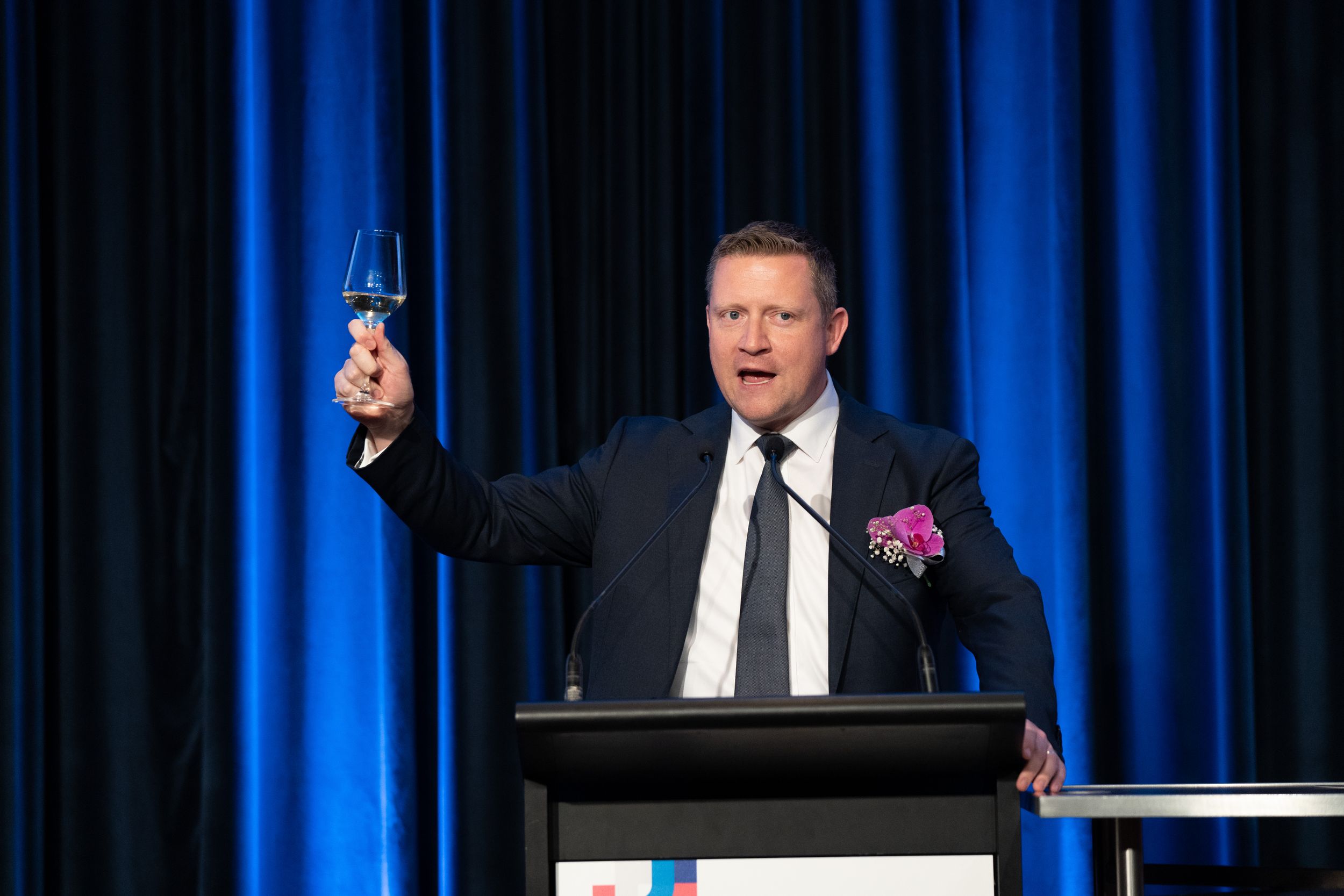 Speaker raises glass while delivering speech at formal podium event.