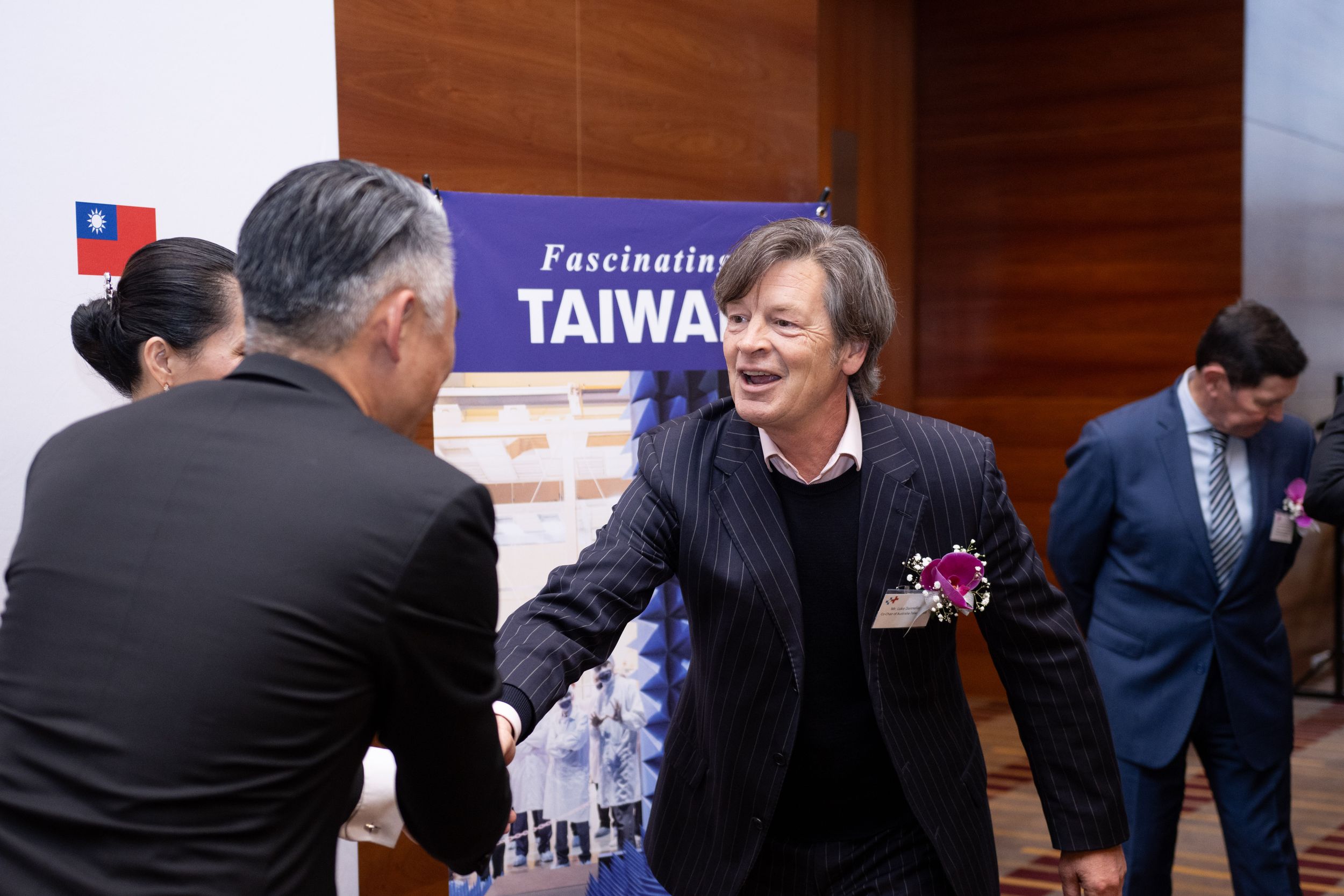 Attendees interact warmly at Taiwan-themed event with promotional backdrop.